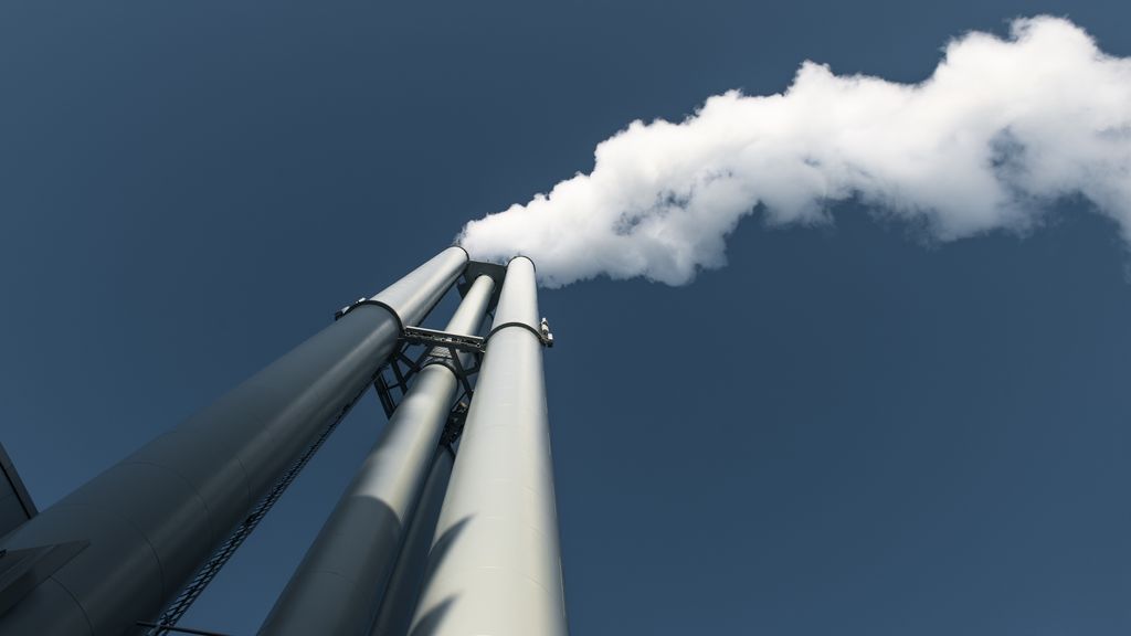 Upward view of factory chimneys releasing smoke into clear sky in Hamburg.