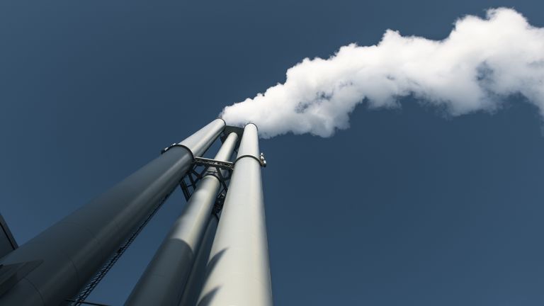 Upward view of factory chimneys releasing smoke into clear sky in Hamburg.