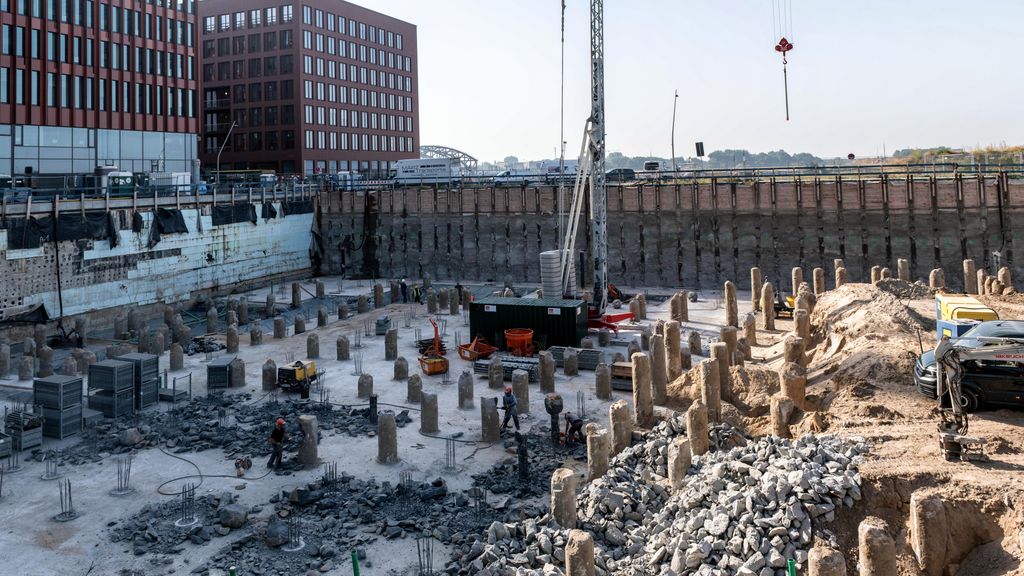 A bustling urban construction site with workers and heavy machinery near tall buildings.