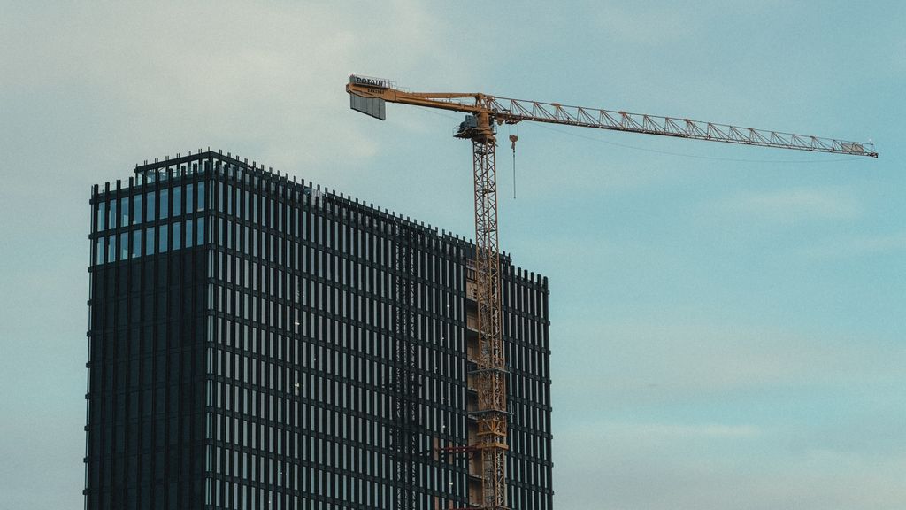 A modern skyscraper under construction with a yellow tower crane against a blue sky.
